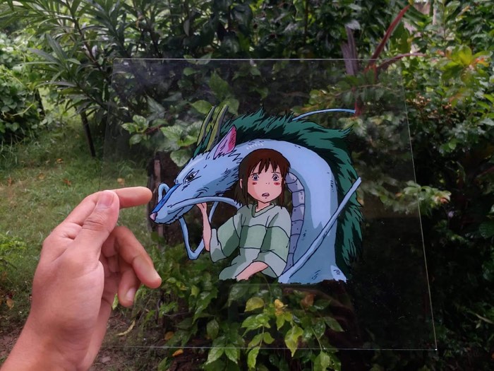 Chihiro and Haku from Spirited Away, painted on a transparent acrylic sheet held up against a garden
